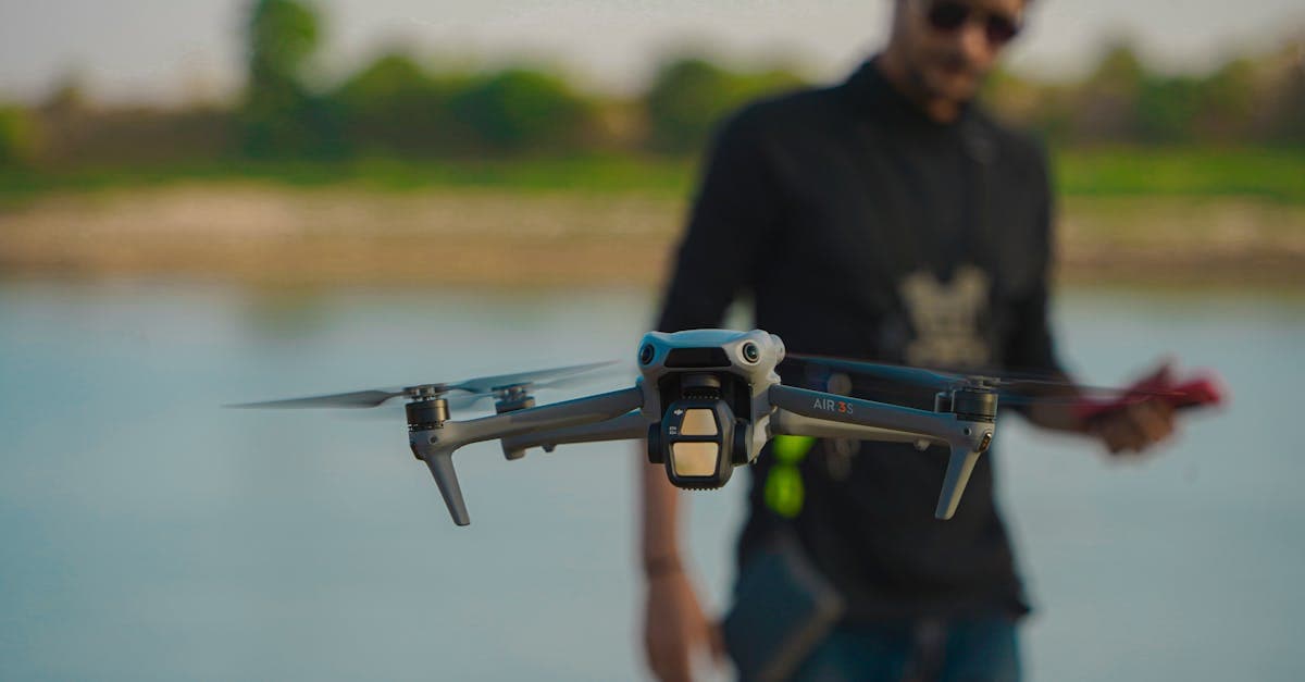 Drone in flight with a field operator standing by a river in rugged outdoor terrain.